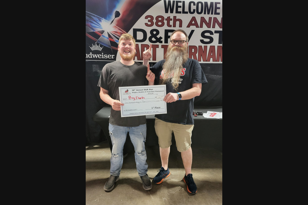 Two men holding a large check at a tournament, one man giving a thumbs up.