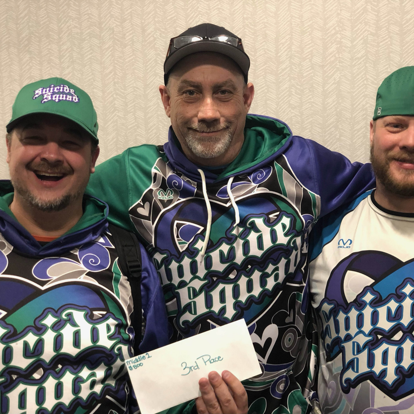 Three men in matching teal and blue patterned hoodies; holding a 