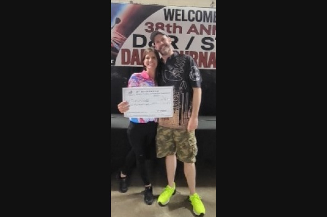 Two people pose with a large check, smiling. A banner reads 