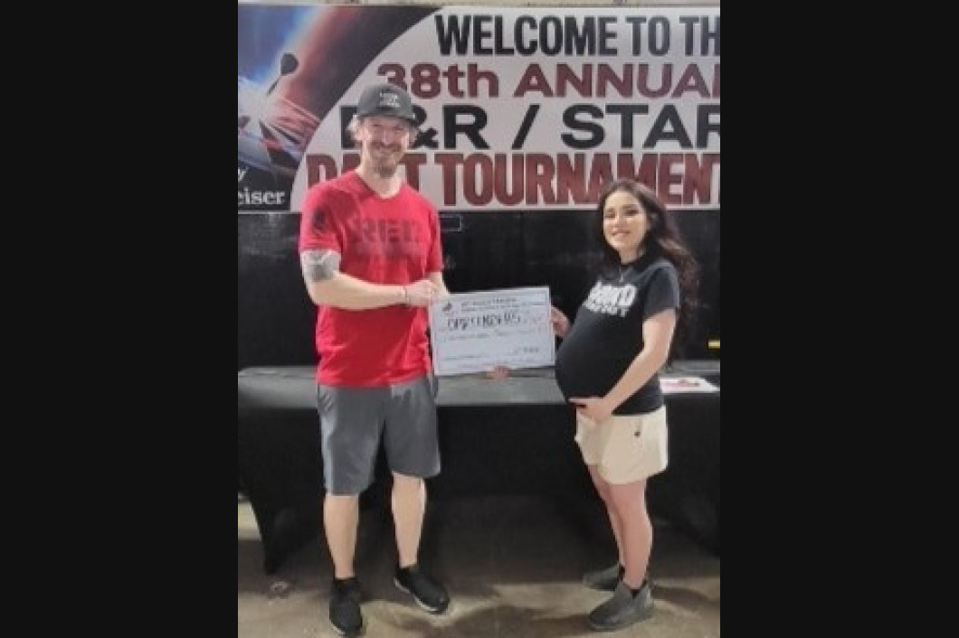 Man in red shirt hands check to pregnant woman at a dart tournament.
