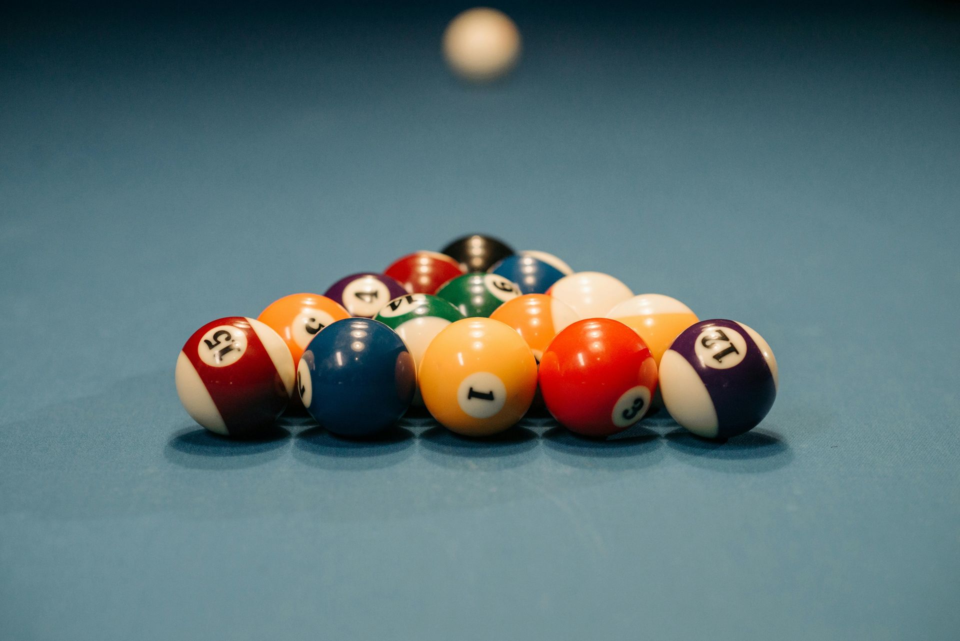 Pool balls racked in a triangle, with the cue ball centered above, on a blue felt pool table.