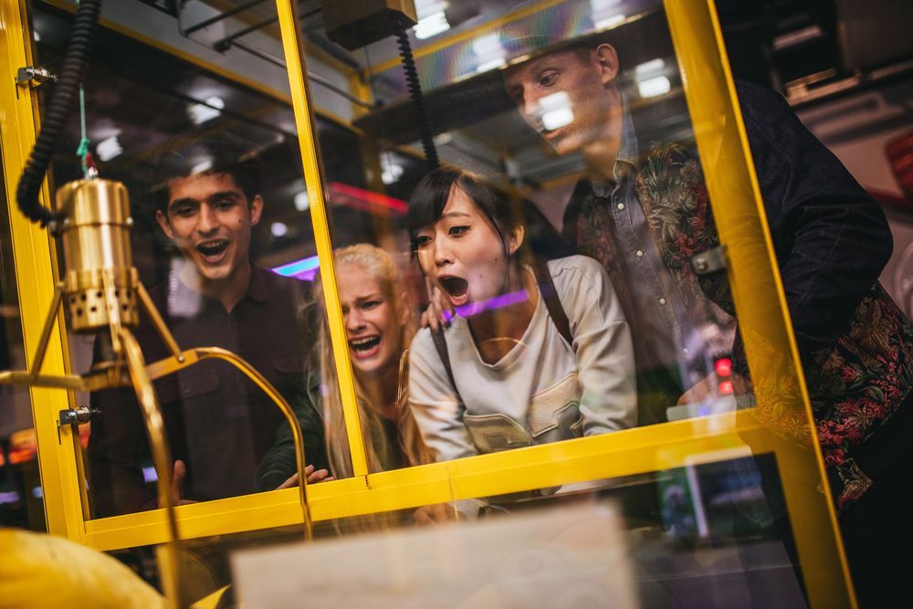 People watch with excitement as a gold-colored machine operates behind glass.