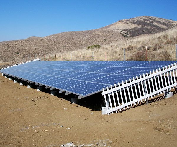 A fence surrounds a field of solar panels with mountains in the background