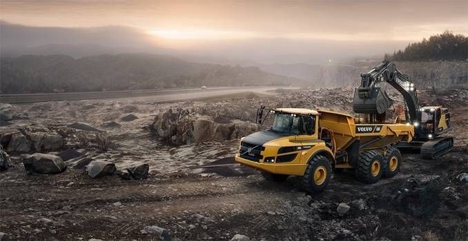 Autocarro articolato giallo ed escavatore in una cava; cielo coperto.