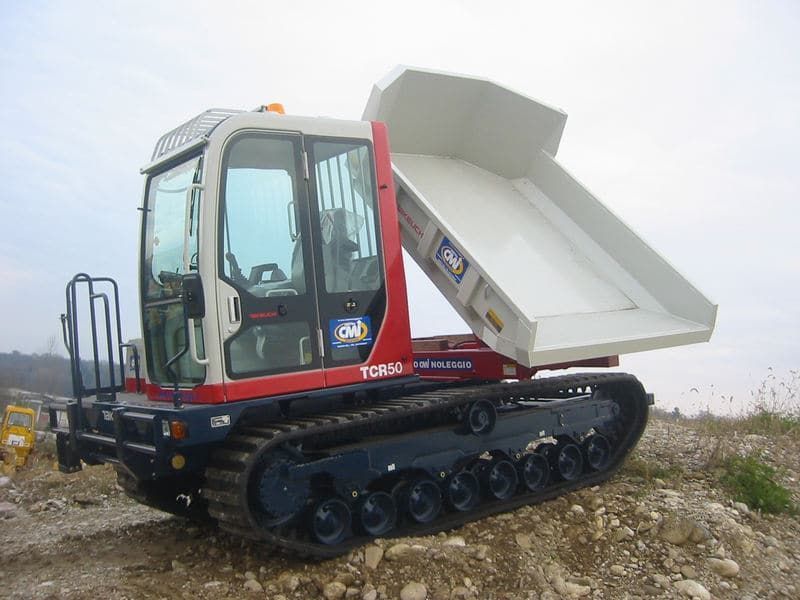 Dumper cingolato bianco e rosso in un cantiere edile; il cassone è sollevato.