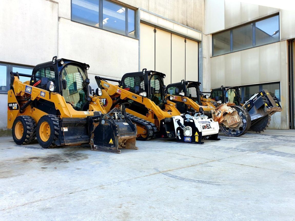 Fila di minipale gialle e nere parcheggiate davanti a un edificio, con vari accessori.
