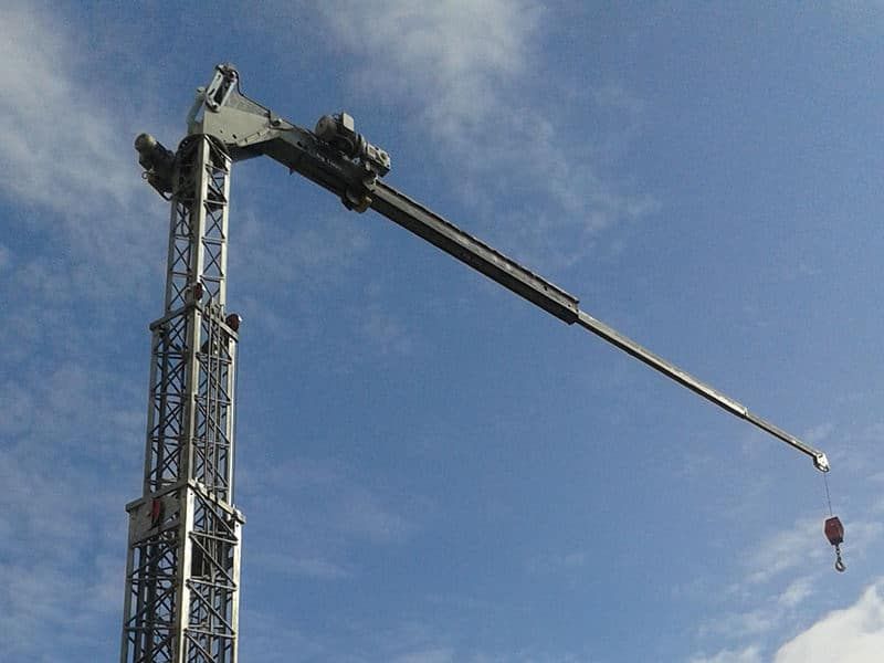 Gru alta con un lungo braccio, posizionata contro un cielo azzurro, con un gancio all'estremità del braccio.