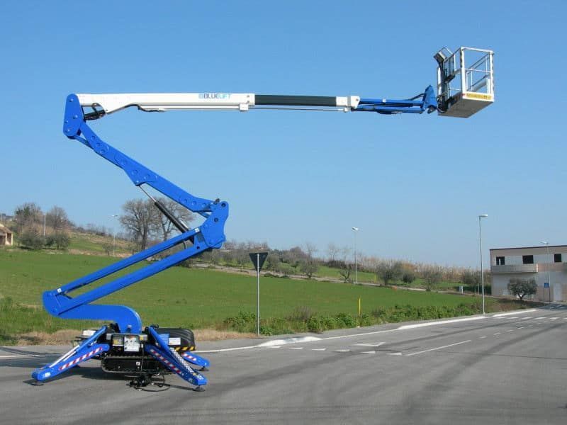 Piattaforma aerea blu estesa su una strada, cesto alla fine; giornata di sole.