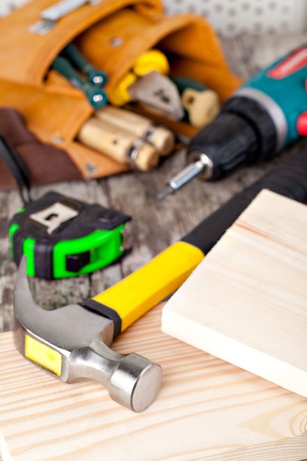Martello, metro a nastro, trapano e assi di legno su un banco da lavoro