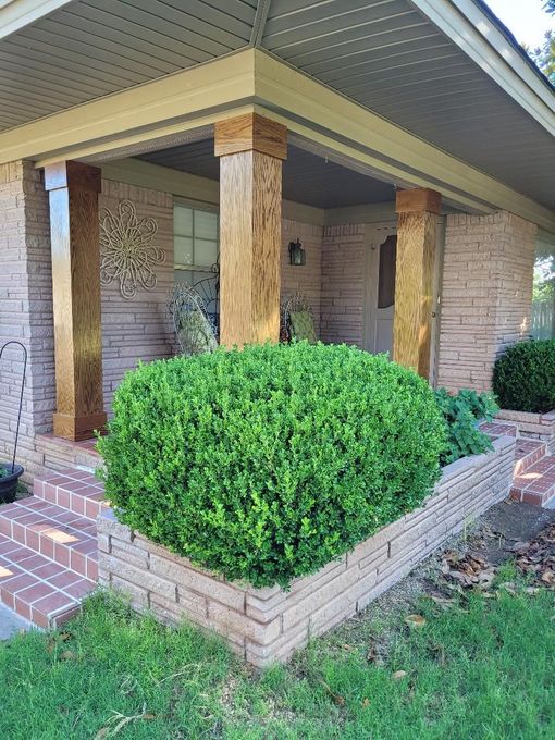 Brick house porch with a trimmed green shrub in the foreground.