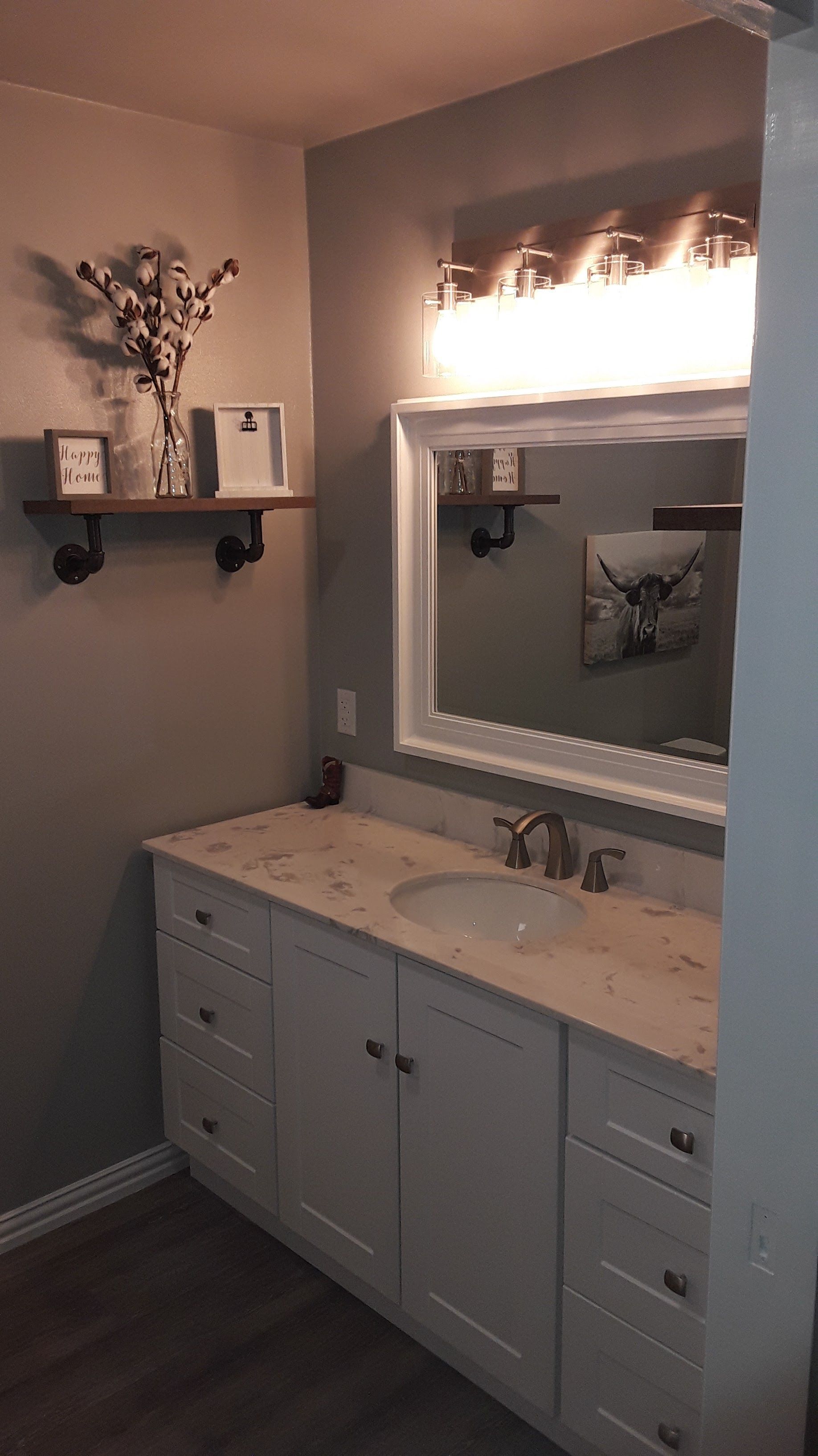 Bright bathroom vanity with white cabinets, marble countertop, large mirror, and wall shelf with decor