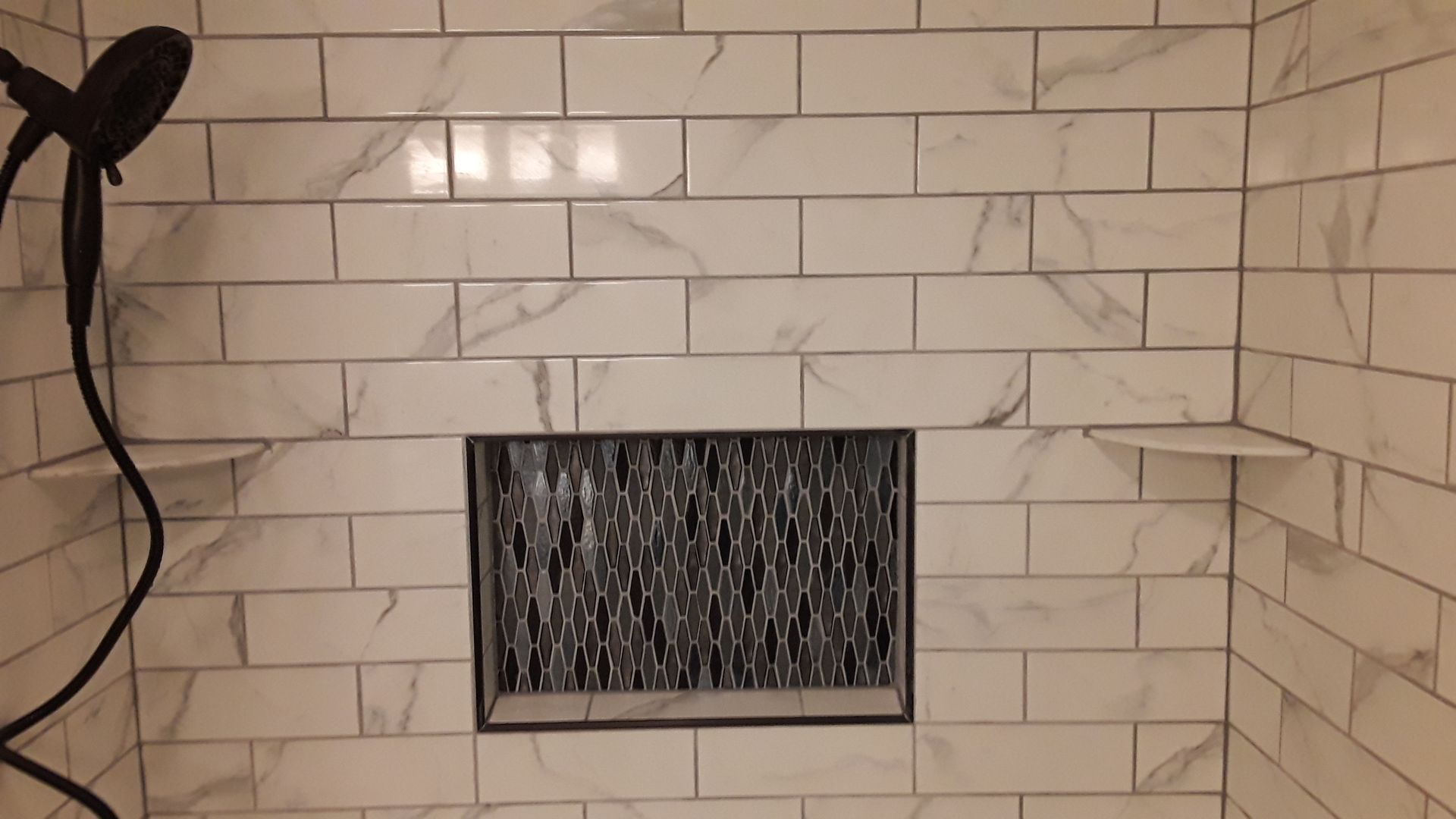 White subway-tile shower wall with a small rectangular frosted glass window and shower hose on the left.