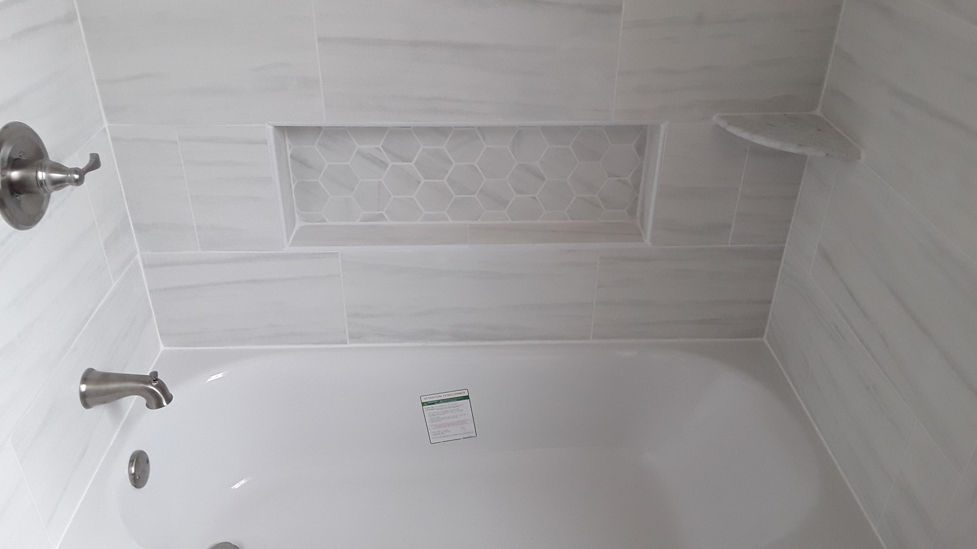 White tiled bathtub with chrome faucet, showerhead, and built-in soap niche.