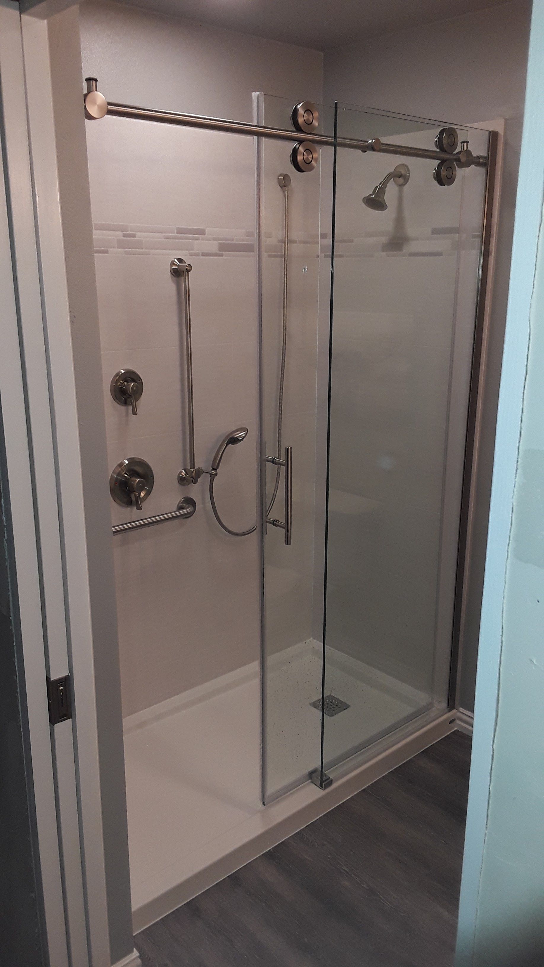 Glass shower stall with chrome hardware, white tile walls, and dark wood-look flooring.