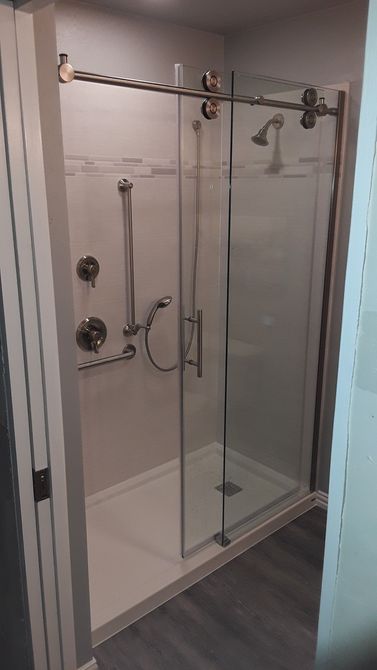 Glass shower stall with chrome hardware, white tile walls, and dark wood-look flooring.