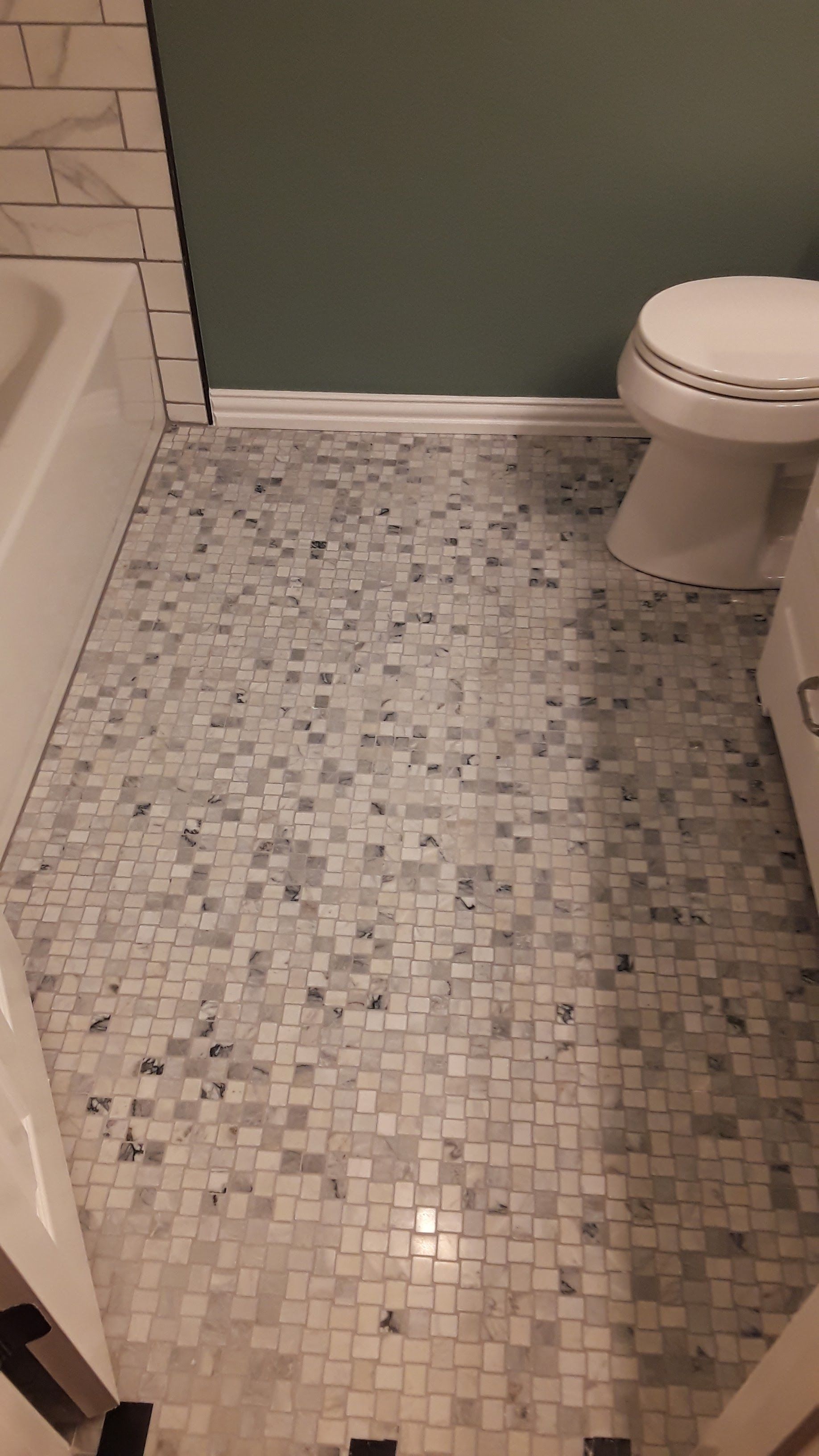 Small bathroom with mosaic tile floor, white toilet, and partial bathtub visible.