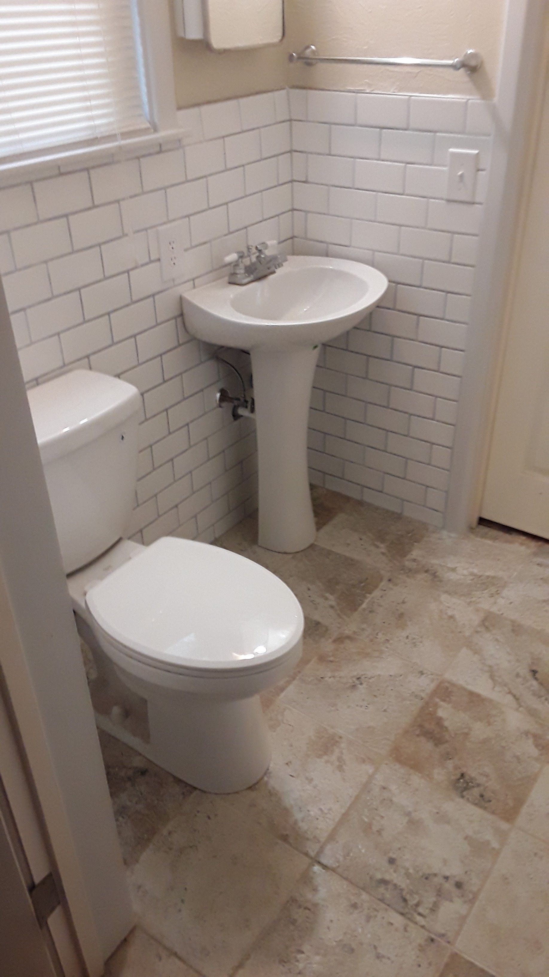Small bathroom with toilet, pedestal sink, white tile walls, and beige floor.