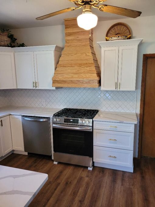 Modern kitchen with white cabinets, stainless stove, stone range hood, and wood floors