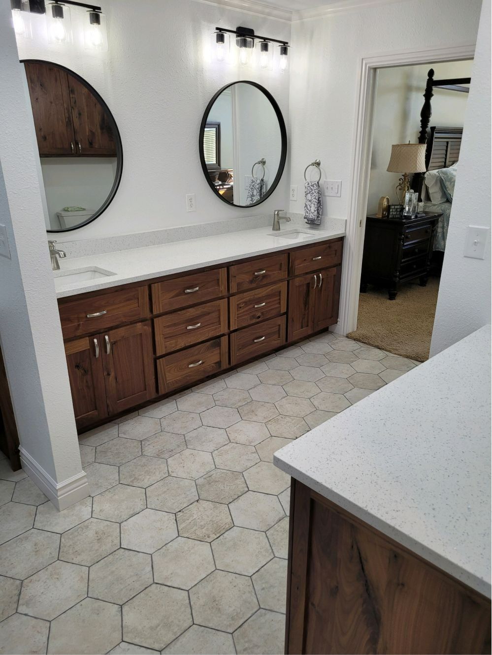 Bathroom vanity with dark wood cabinets, round mirrors, white countertops, and hex tile floor.