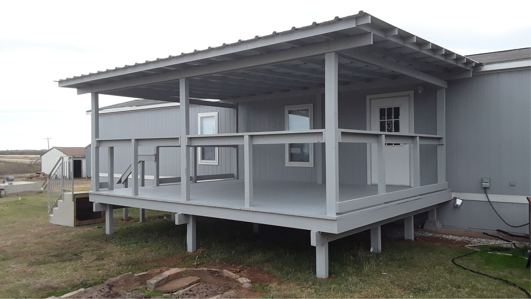 Gray porch attached to a house, with ramp-like railings and metal roof in a grassy yard