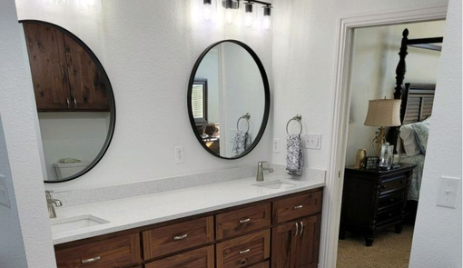 Bathroom vanity with dark wood cabinets, white countertop, and two round mirrors next to a doorway