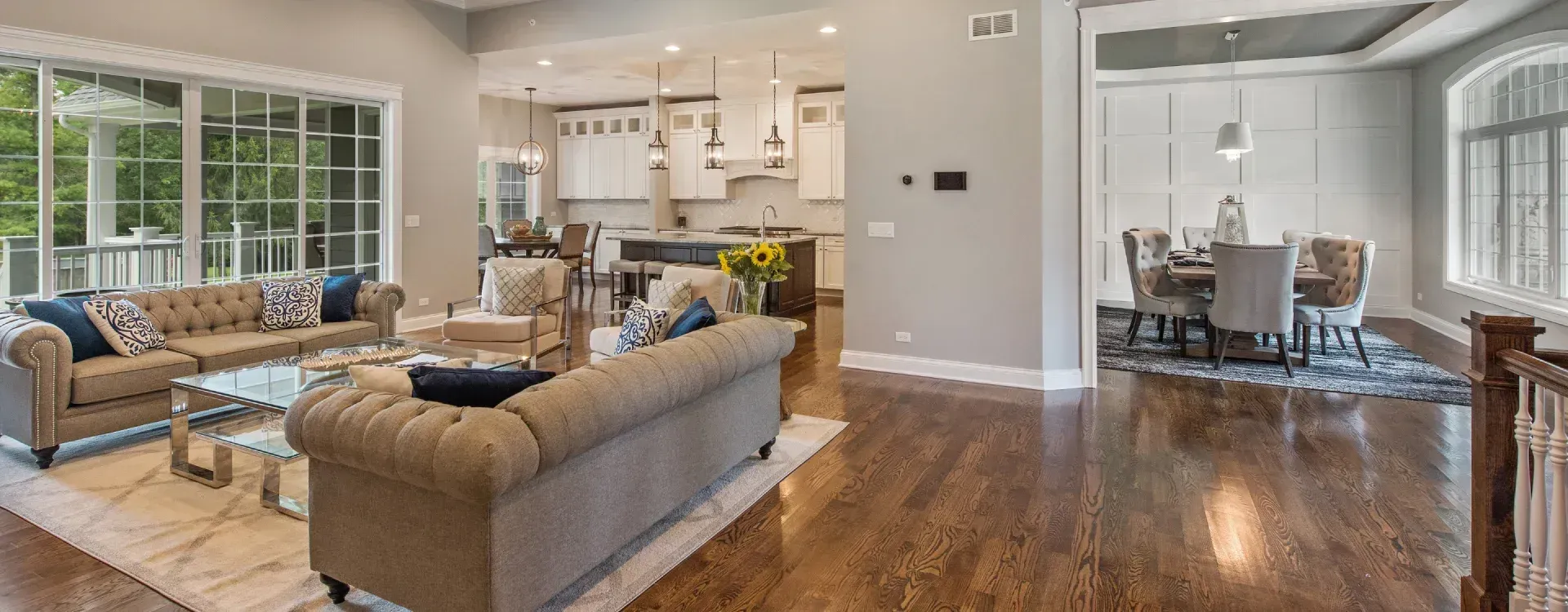 Bright open-concept living room and dining area with hardwood floors, beige sofas, and large windows