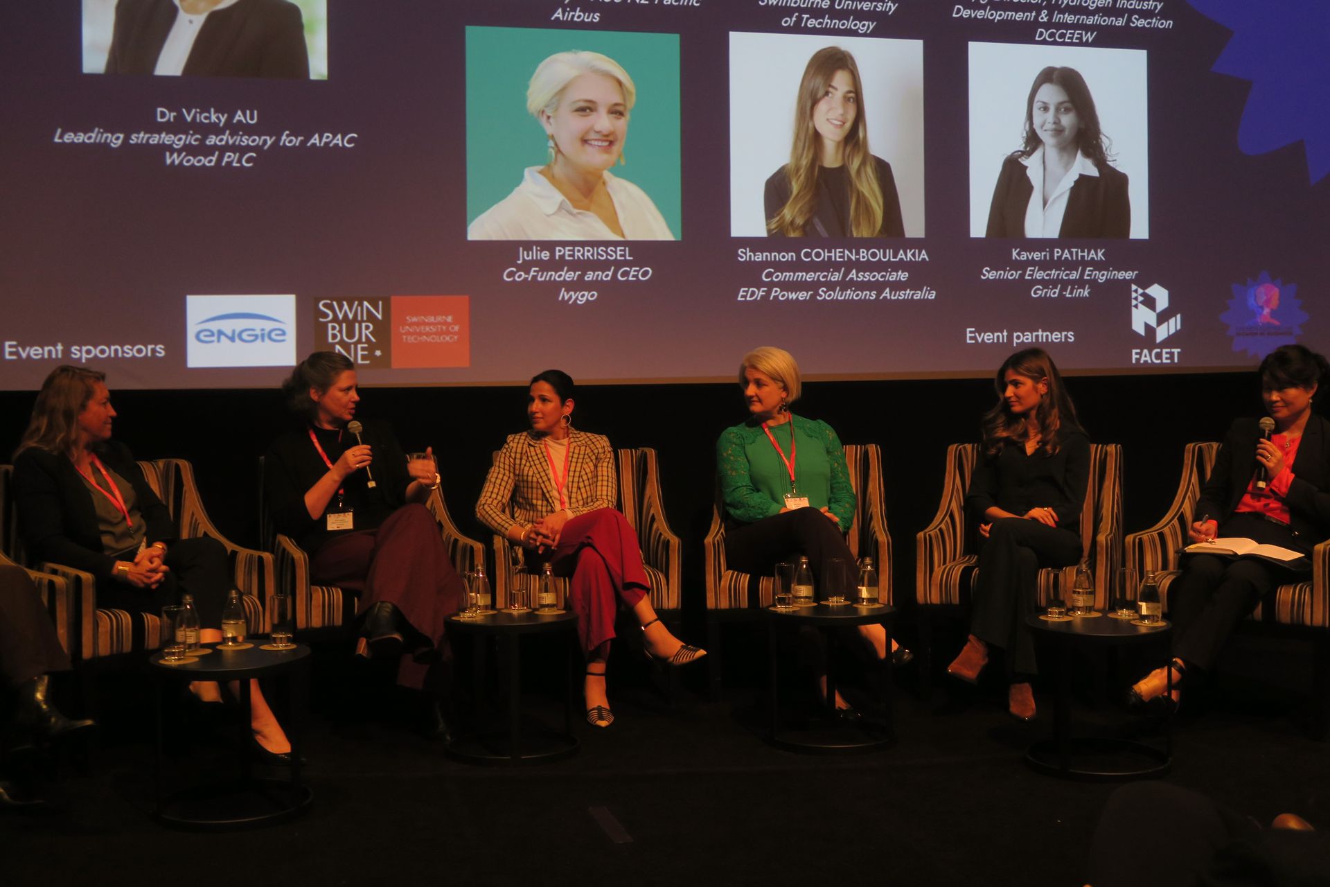 Panel of women seated, discussing on stage. Panelists, headshots, and sponsor logos visible.