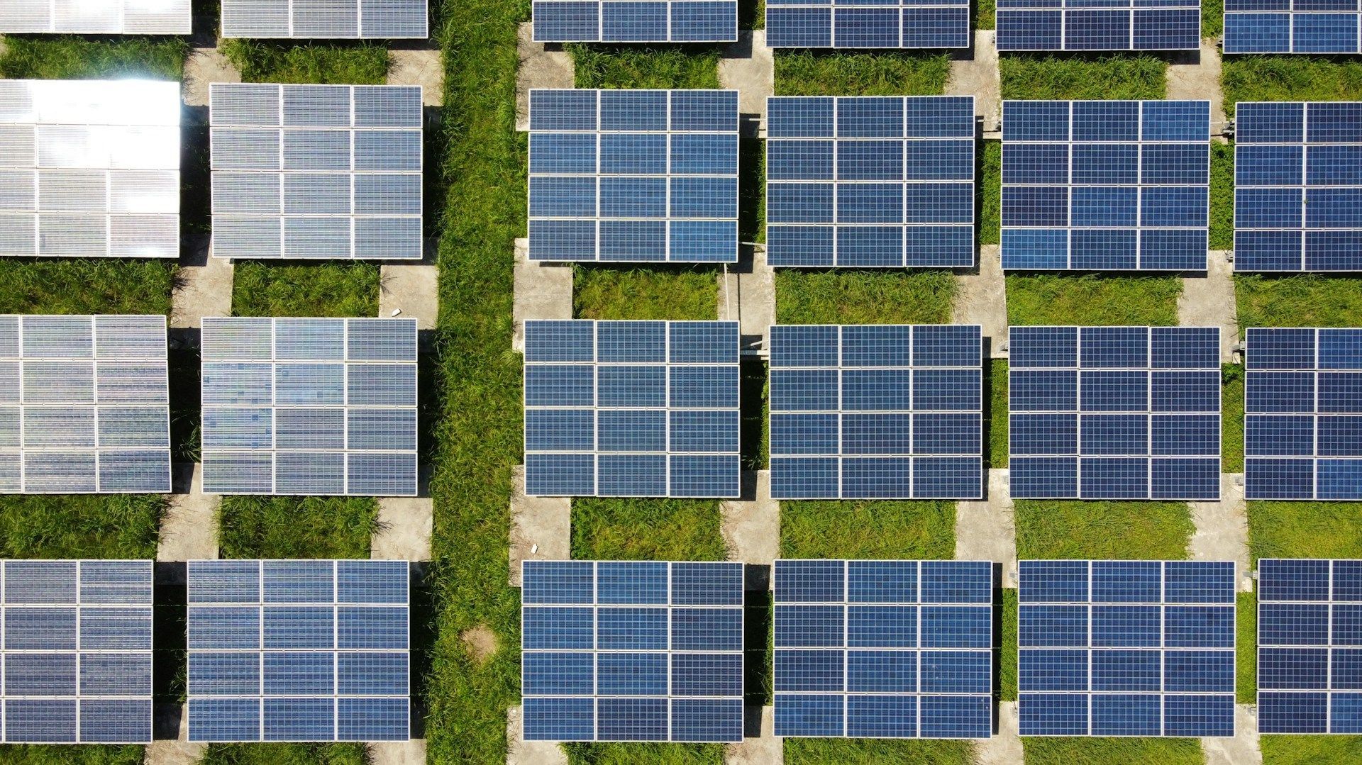 An aerial view of a row of solar panels sitting on top of a lush green field.