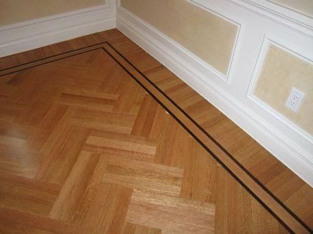 Wooden parquet floor corner with dark border trim beside a cream wall and white molding