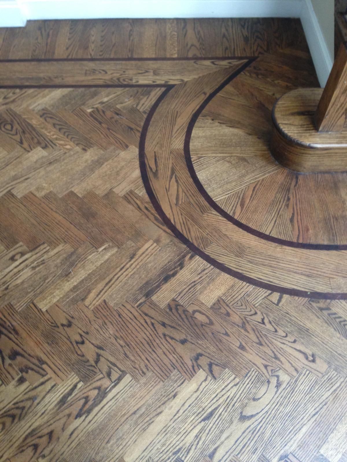 Wooden parquet floor with circular dark inlay pattern around a round base near the wall