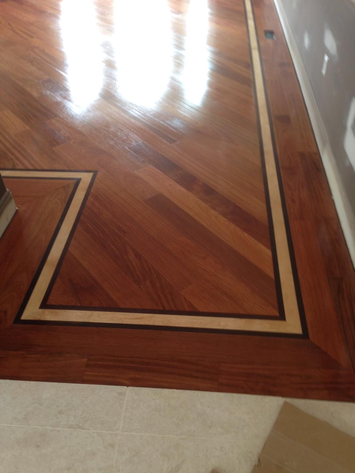 Polished hardwood floor with dark border inlay and bright window reflections.