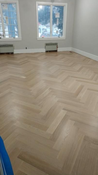 Empty room with herringbone wood floor, two windows, and white walls.