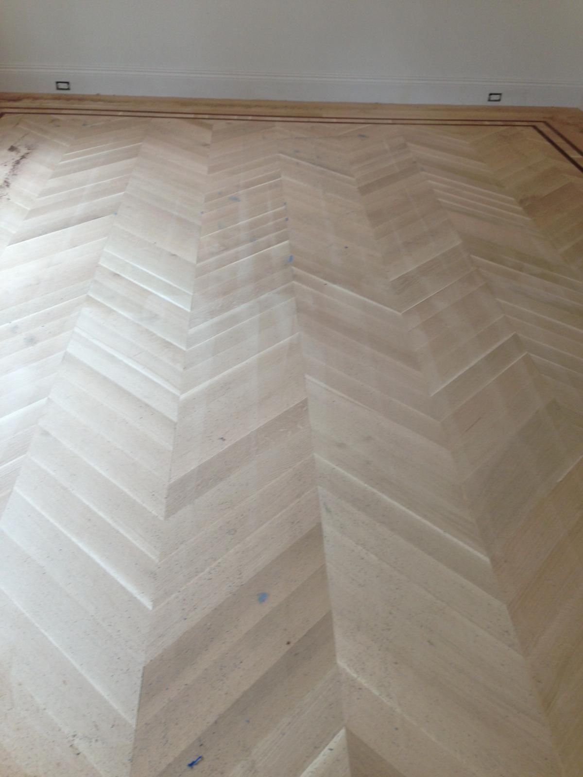 Light wood herringbone floor meeting a white wall and baseboard.