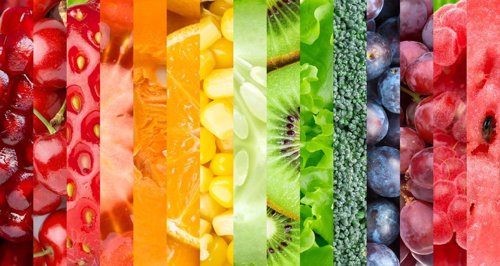 Strisce di frutta e verdura dai colori dell'arcobaleno, tra cui ciliegie, arance, mais, kiwi, broccoli, uva e anguria.