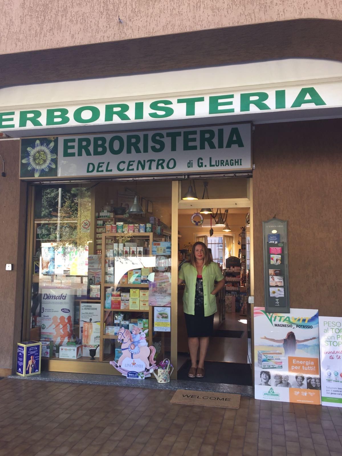 Due donne sorridenti dietro il bancone di una farmacia con scaffali pieni di prodotti.