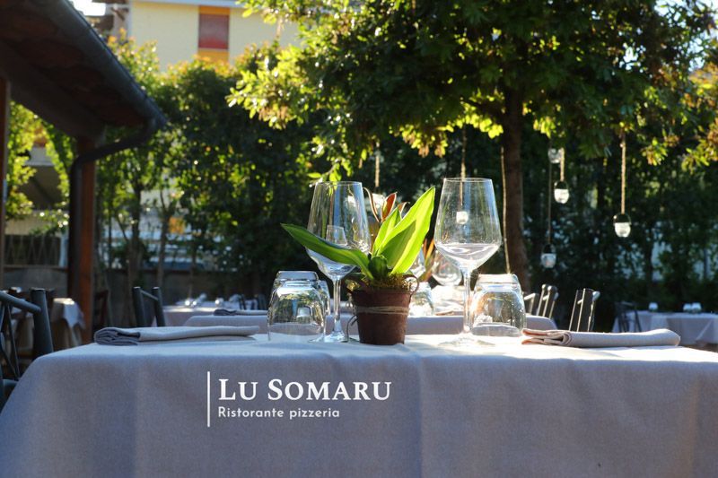 un tavolo con bicchieri e un vaso di fiori è allestito per il lu somaru ristorante pizzeria