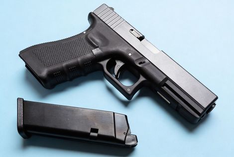 A black and silver semi-automatic pistol with a detached magazine, lying on a plain light blue background.