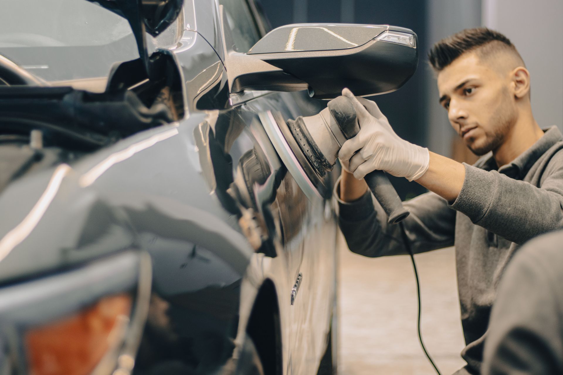 Detailing technician polishing a gray car with a buffer in a garage
