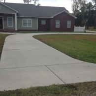 A curved concrete driveway leads to a single-story home featuring a combination of light-colored siding and red brick.