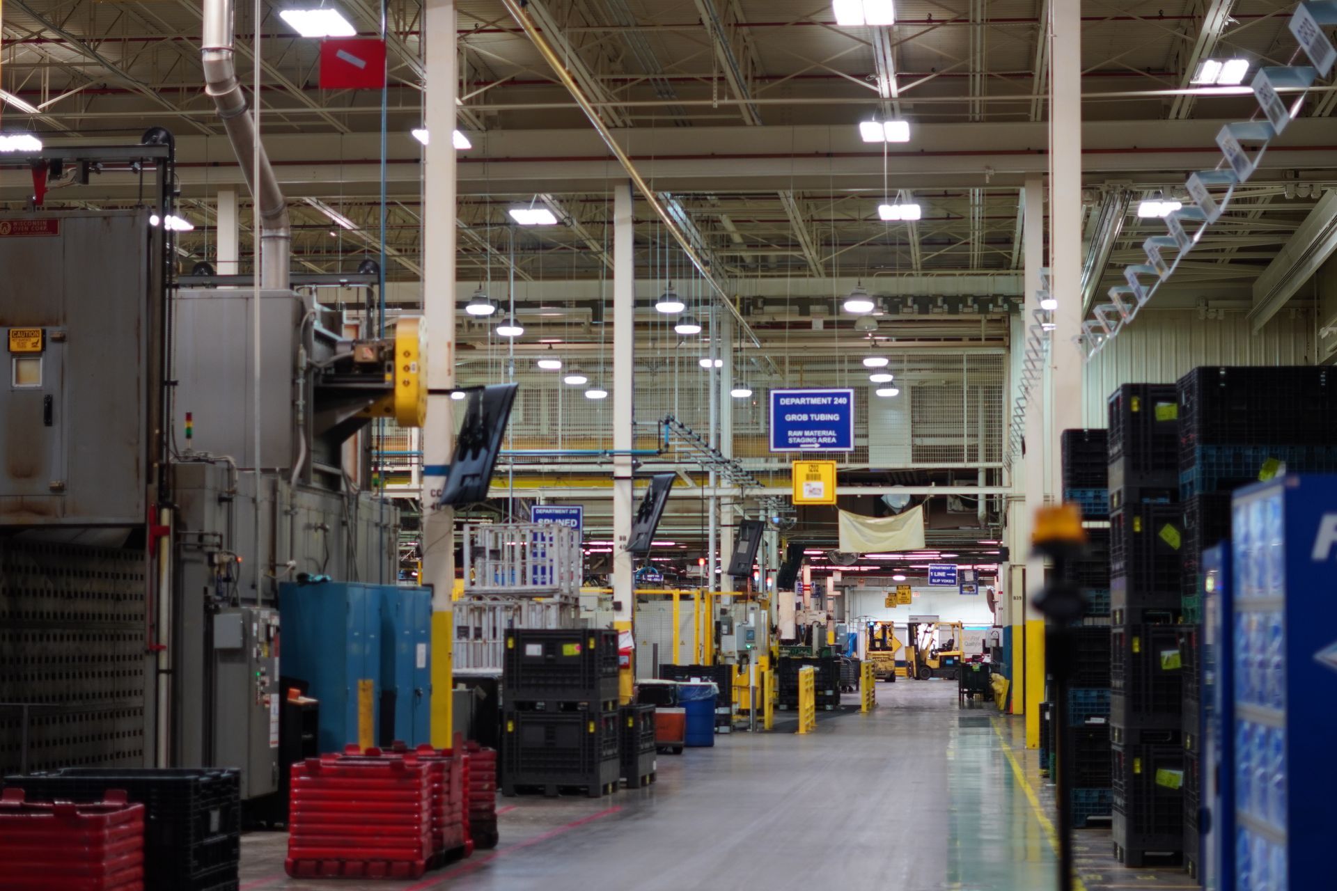 Warehouse interior with machinery, stacks of containers, and a forklift operator.