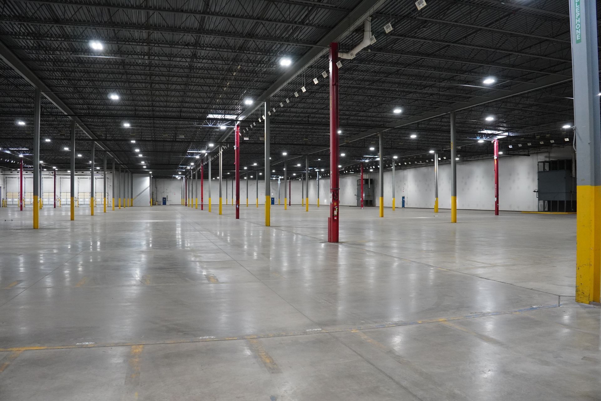 Empty warehouse interior with concrete floor, metal beams, and overhead lights.