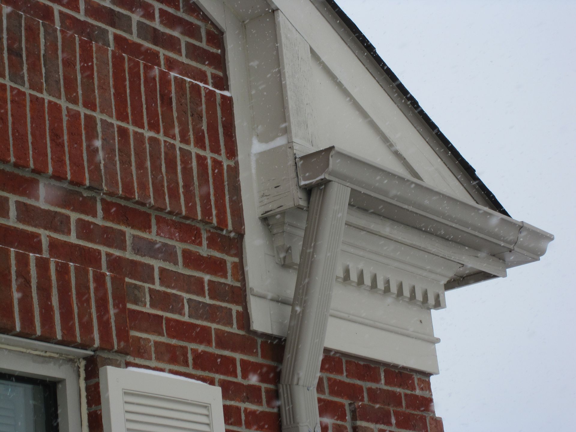 Red brick building corner with white trim, gutter, and falling snow.