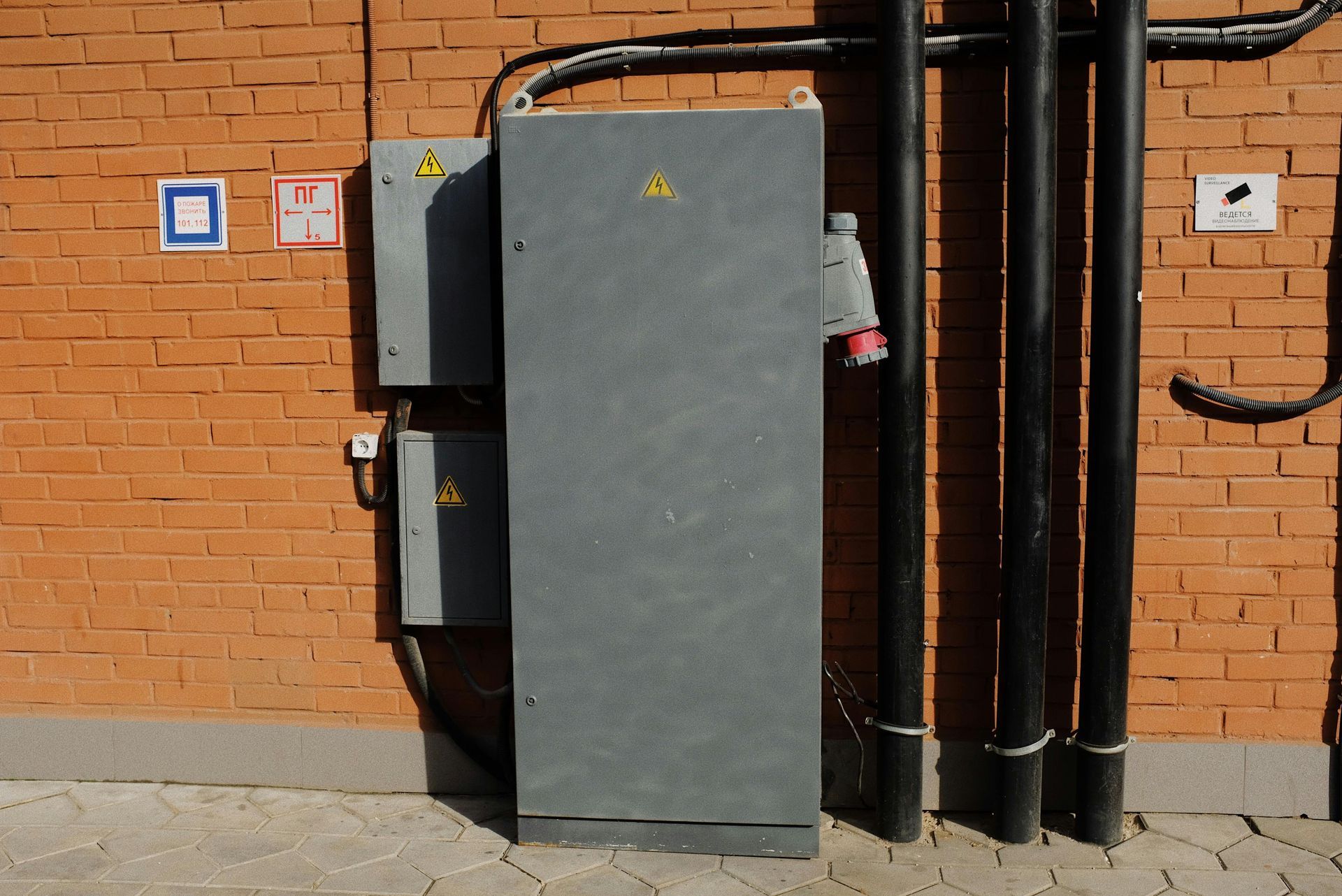 Electrical box and conduit on brick wall, warning signs present.