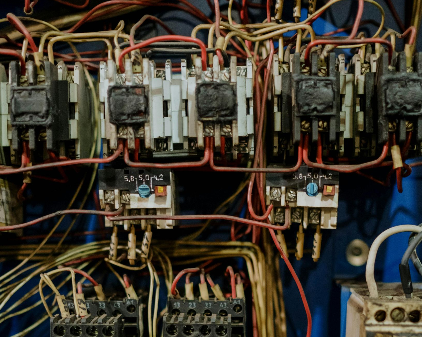 Close-up of a tangled electrical panel with wires and relays; some parts appear damaged.