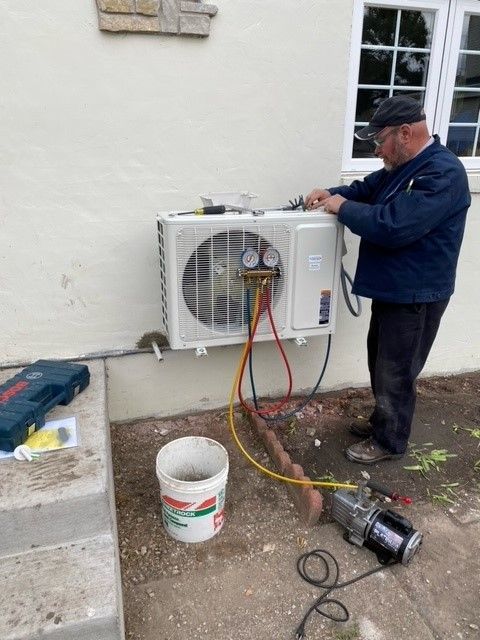 HVAC technician servicing an outdoor air conditioning unit. He's using gauges and hoses.
