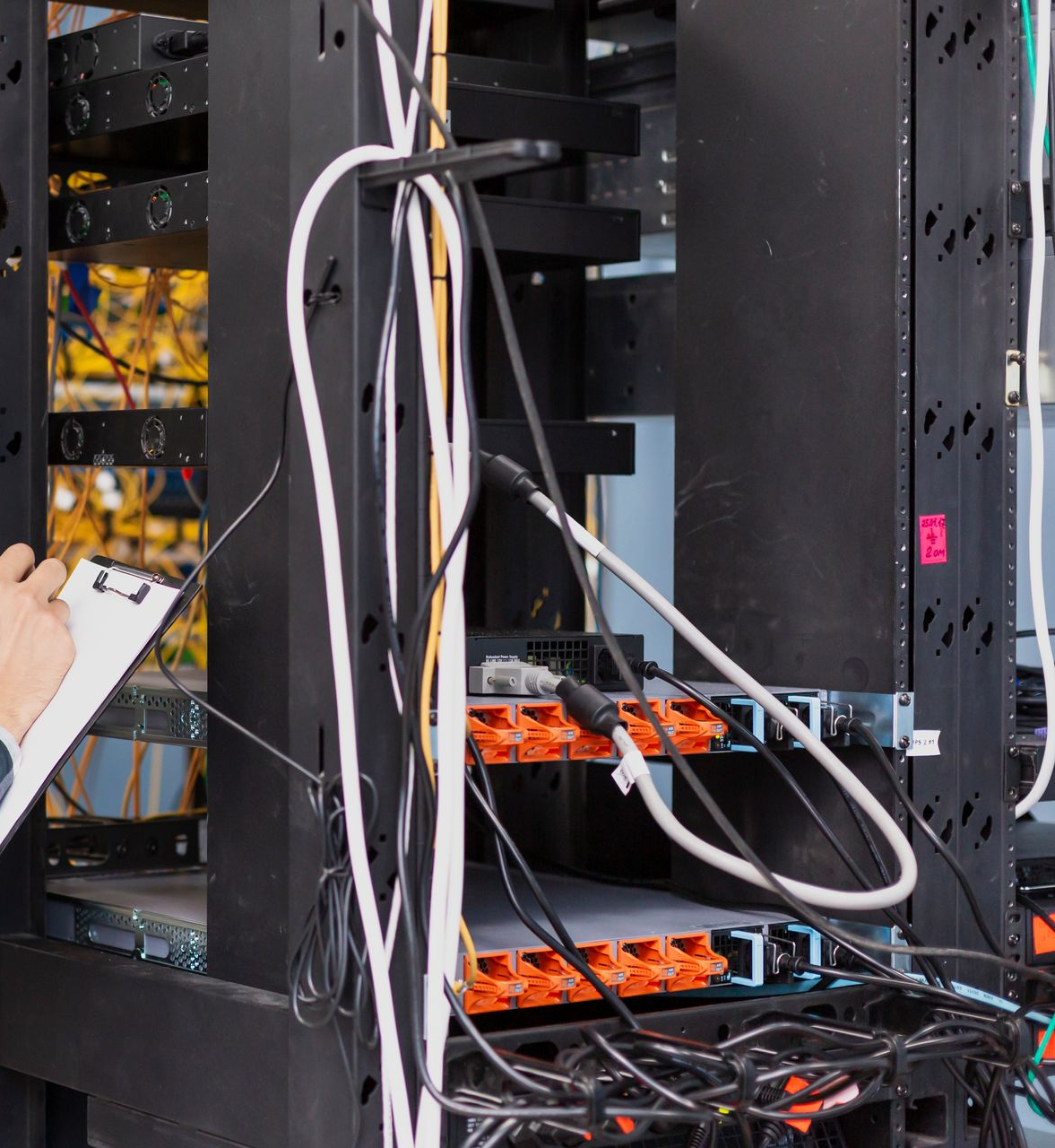 Person examines server rack with cables, orange switches.