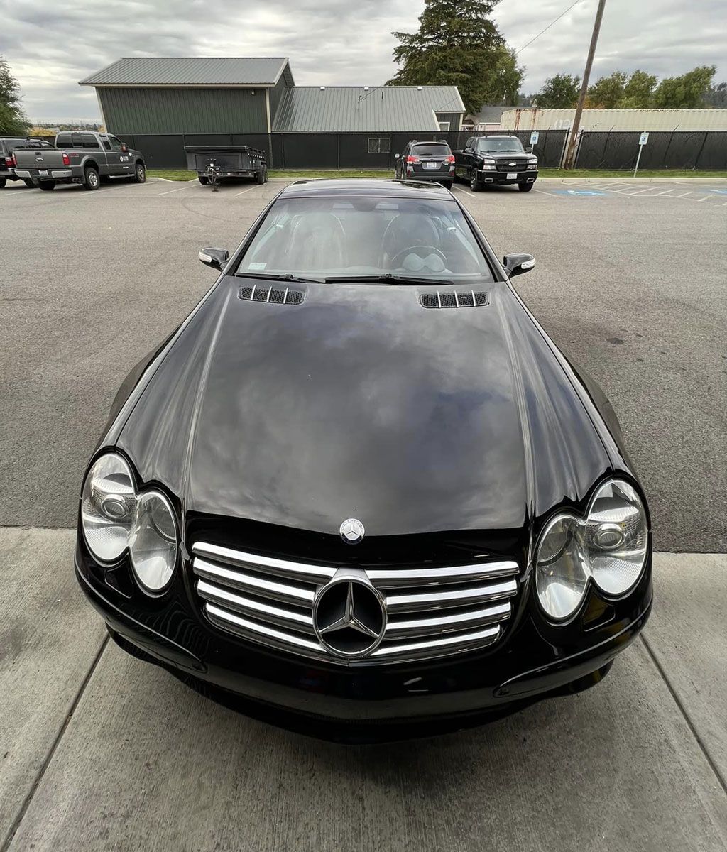 Black Mercedes-Benz SL-Class car parked in a lot, with a building in the background.