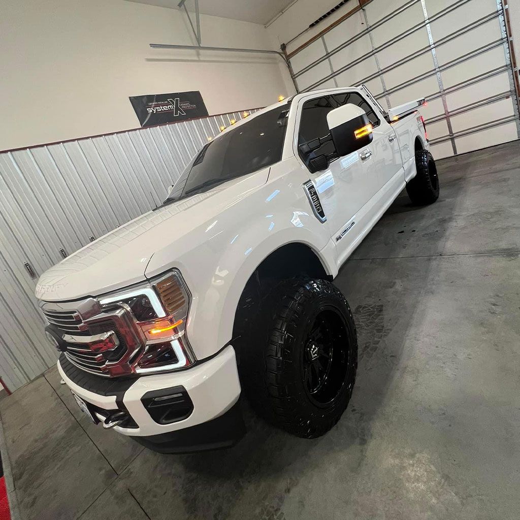 White lifted truck with black wheels parked inside a garage.