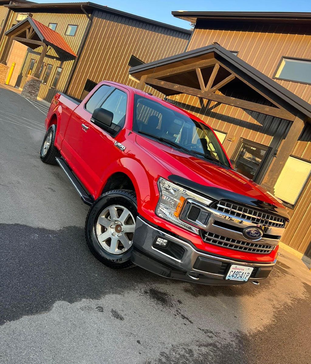 Red Ford F-150 pickup truck parked near a brown building with a sloped roof.