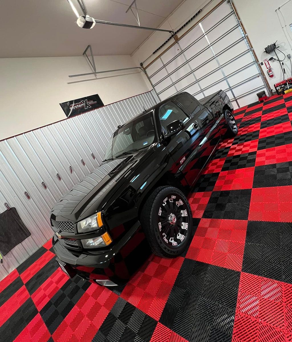 Black pickup truck parked in a garage with red and black checkered flooring.